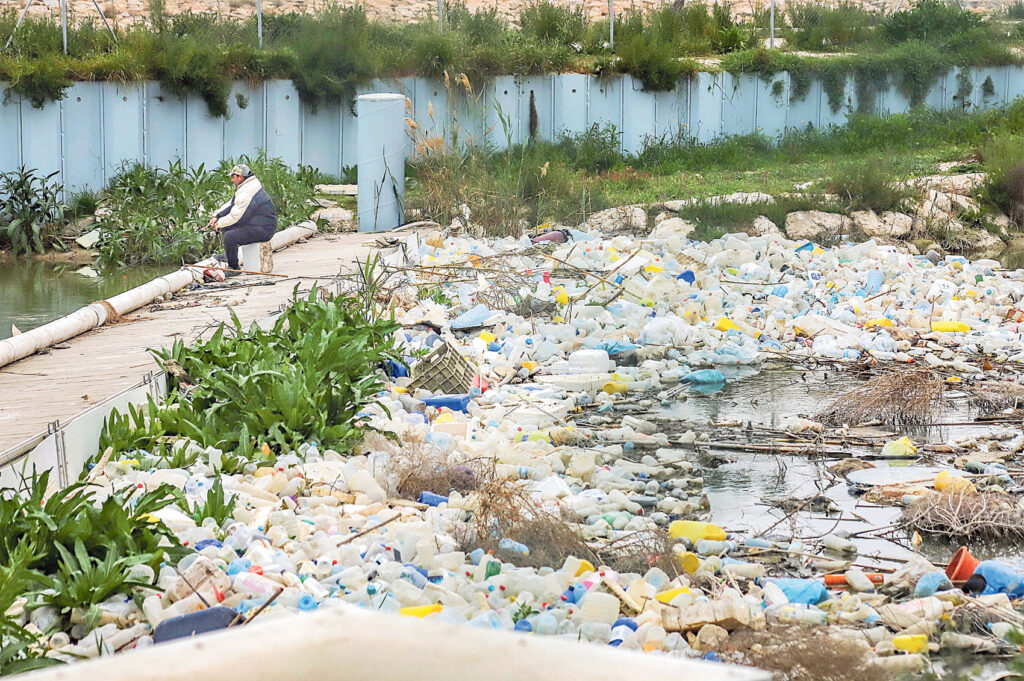 Un hombre pesca con caña junto a una gran acumulación de plásticos en Alicante.